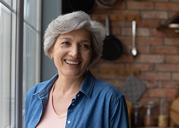 Woman in blue shirt standing by kitchen window smiling